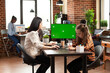 © DC Studio - Caucasian mother and daughter sitting at table with computer monitor displaying greenscreen. In startup office, businesswoman using desktop pc with isolated mockup template as little kid sits nearby.