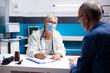 © DC Studio - Elderly physician discusses healthcare treatment options with senior white male patient seated in clinic office. Retired doctor attentively listening to concerns of old man and writing on clipboard.