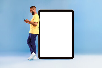 Wall Mural - attractive african american man standing near huge digital tablet with empty white screen, using sma
