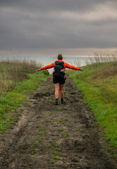 Wall Mural - Hiker In Orange Coat Traverses Muddy Path With Arms Extended