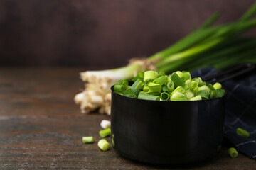 Wall Mural - Chopped green onion in saucepan on wooden table, closeup. Space for text