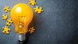 © sarinya - Bright Yellow Light Bulb Surrounded by Puzzle Pieces on Gray Background