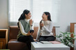 © Crystal - Two young asian women laughing and chatting on a sofa in their apartment
