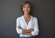 © muhammadarslan - Portrait of a smiling business woman standing with arms crossed on a grey background, wearing a white shirt and jeans. A female entrepreneur