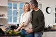© peopleimages.com - Happy, couple and cooking in home with support for salad recipe, vegetable preparation and bonding together. Kitchen, mature people or affection with dinner meal, healthy food or love in relationship