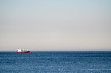 Cargo ship sailing across a calm ocean under a clear sky during the day