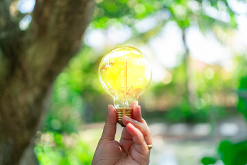 Hand holding a light bulb with glowing light on a blurred outdoor background. Bright idea, creativity and innovation concept.