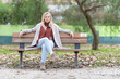 © KONSTANTIN SHISHKIN - Young woman relaxing on park bench in autumn