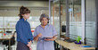 © Raushan_films - Indian senior old elder boss women lady standing hold book file make new project indoor office young adult expert intern girl older staff do work talk day task read report share ideas plan job place