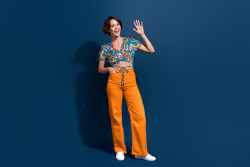 Wall Mural - Full body photo of pretty young girl waving hand hello greeting dressed stylish flared pants outfit isolated on dark blue color background