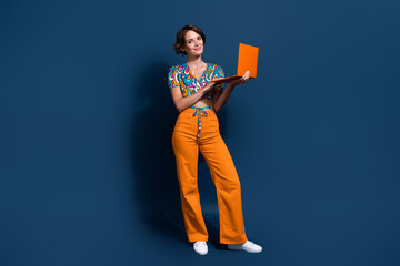 Full length photo of lovely young lady hold netbook working remotely dressed stylish flared pants isolated on dark blue color background