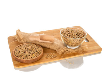 Wall Mural - Raw lentils in a glass plate and wooden saucer with a wooden spoon on a wooden kitchen board, isolated on a white background, macro.