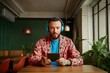 © Sergio - Young man with headphones engaged in digital device activity indoors at trendy cafe with greenery
