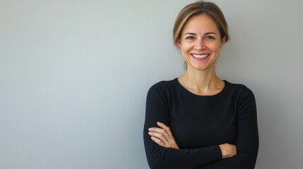 Wall Mural - smiling woman in black long-sleeve top with arms crossed standing against light gray background expressing confidence and happiness