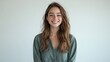 © The 2R Artificiality - Smiling young adult woman with long wavy hair wearing green shirt and jeans standing against a soft white background showcasing natural beauty and joy