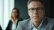 © The 2R Artificiality - Middle-aged professional businessman in glasses engaged in serious discussion with diverse colleagues in modern office boardroom setting.