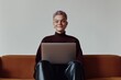 © Sergio - Young adult with purple hair working on laptop while sitting on couch in modern indoor space