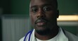 © ABCreative - In a hospital setting, a young African physician poses with a warm smile, stethoscope draped around his neck, and dressed in a white coat.