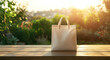 © Саша Федюк - A blank white tote bag rests on a wooden table outdoors during golden hour, with lush greenery in the background and sunlight filtering through