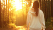 © Bonsales - Back view of a young woman wearing a hoodie, enjoying a peaceful walk in a forest at sunset, embracing the tranquility of nature as the golden light filters through the trees