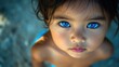 © The 2R Artificiality - toddler with striking blue eyes gazing upwards at a beach in Thailand captured in warm sunlight with sandy background and water reflections
