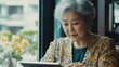 © The 2R Artificiality - Senior woman with silver hair using tablet in modern office with large windows, warm tones, vibrant yellow flowers on desk, focused expression