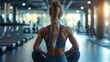 © KarpenArt Studio - A woman with long blonde hair is sitting on the floor of a gym or exercise room, wearing a gray sports bra and leggings.