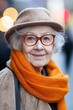 © StockUp - A smiling elderly woman wears a cozy orange scarf and a chic hat against a blurred background.