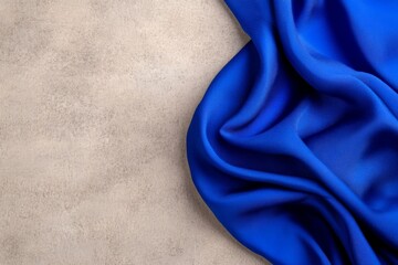 Fototapete - A vibrant blue silk piece folded elegantly on a textured beige surface creates a striking contrast, offering ample copy space for design purposes