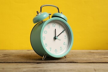 One turquoise alarm clock on wooden table against yellow background