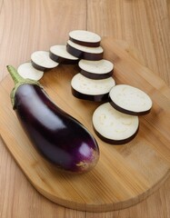 Wall Mural - A vibrant purple eggplant sits beside its sliced counterparts on a light wood cutting board.