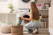 © Pixel-Shot - Woman with wicker basket putting clothes into washing machine in laundry room, back view