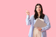 © Pixel-Shot - Beautiful young happy woman with laptop pointing at something on pink background