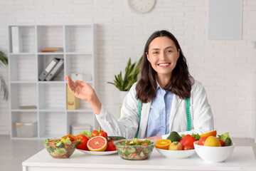 Wall Mural - Young female nutritionist with healthy food on table in office