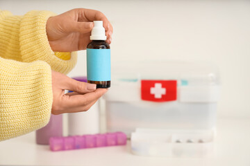 Poster - Woman holding bottle of drops against first aid kit at home, closeup