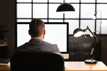 Wall Mural - Young businessman working with blank computer in office at night, back view