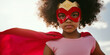 © Flux Imagery - Niña afro con capa roja y antifaz con un disfraz de superheroina durante carnaval