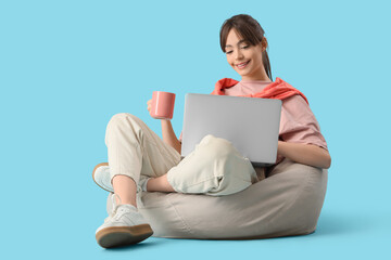 Canvas Print - Teenage girl with coffee cup and laptop working online on blue background