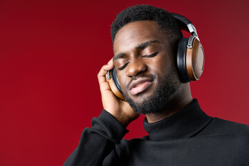 Young African man enjoying music with headphones, expressing joy and relaxation against a vibrant red background Perfect for lifestyle and music related concepts