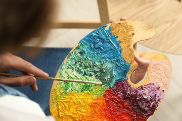 Wall Mural - Man with paintbrush mixing paints on palette indoors, closeup