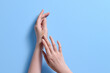 © Marc Tran/Stocksy - Woman Applying Cream to Hands on Blue Background