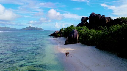 Wall Mural - Discover a secluded beach in Seychelles, where gentle waves meet golden sands. Enjoy the tranquility as two figures stroll along the shoreline under a bright blue sky, Anse Source D'Argent La Digue 