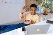© Jimena Roquero/Stocksy - Young man eating cereals while doing video call on laptop
