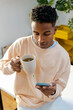 © Jimena Roquero/Stocksy - Young entrepreneur in office drinking tea while checking smartphone