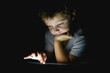 © Nasos Zovoilis/Stocksy - Child engaged in focused activity with mobile device in darkness