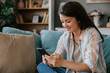 © Mihajlo Ckovric/Stocksy - Happy Woman Relaxing on Couch Browsing Smartphone at Cozy Home