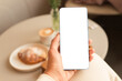 © Evgeniia Siiankovskaia/Stocksy - Woman's hand holding mobile phone with blank screen at cafe.