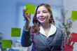 © amnaj - Businesswoman planning strategy using sticky notes and writing on glass board in office