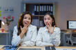 © amnaj - Two surprised businesswomen covering their mouths with hands in office at night