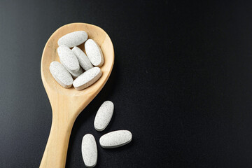 Wall Mural - white Pills Medicine tablet capsules in a wooden spoon blister pack on a black background